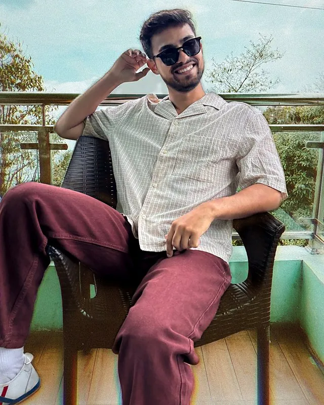 Aman laughing on a balcony chair in sunglasses